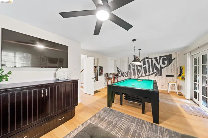 Recreation space featuring wood-finish flooring, a ceiling fan with integrated lighting, a wall-mounted display, and white French doors