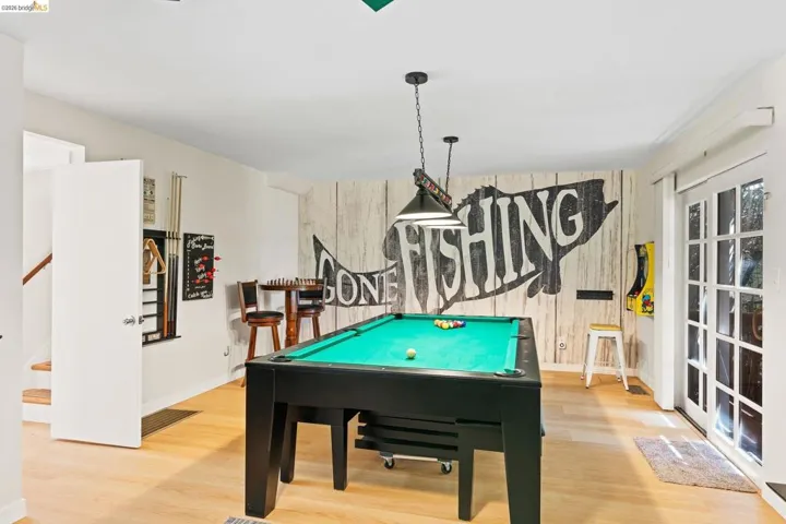 Recreation room featuring wood-finish flooring, a decorative accent wall, recessed lighting, and French doors providing external access