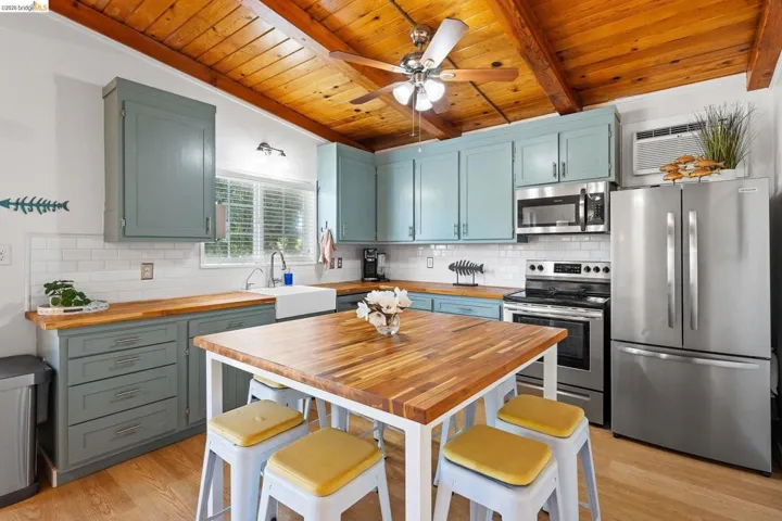 Kitchen featuring a rustic wood-planked ceiling with exposed beams, light blue cabinetry, white subway tile backsplash, wood-finish countertops, and stainless steel appliances