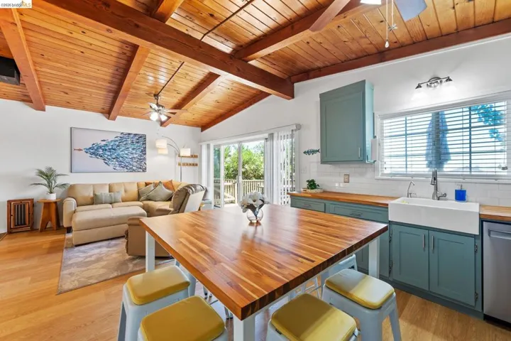Open concept living space featuring a vaulted wood-plank ceiling with exposed beams, wood-finish flooring, a kitchen with custom-painted cabinetry, wood countertops, and a farmhouse sink