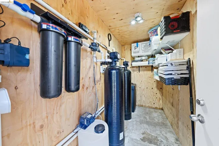 Dedicated utility room featuring wood-finish wall paneling, a concrete floor, and multiple water filtration systems