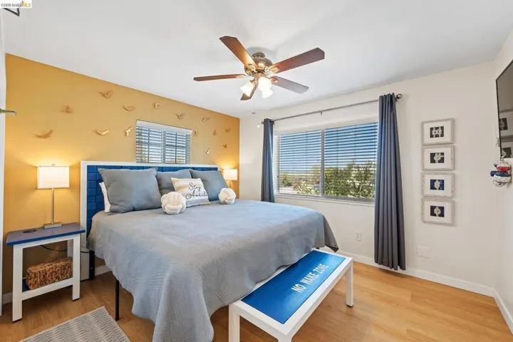 Bedroom featuring a ceiling fan with integrated lighting, a window with horizontal blinds and drapes, and wood-finish flooring