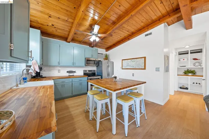 Kitchen featuring wood-finish flooring, vaulted wood-paneled ceiling with exposed beams, light blue cabinetry, butcher block countertops, and white subway tile backsplash