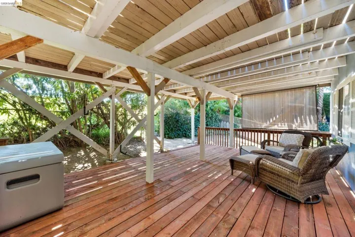 Spacious covered wood deck with exposed beam ceiling, white support columns, and wood plank flooring