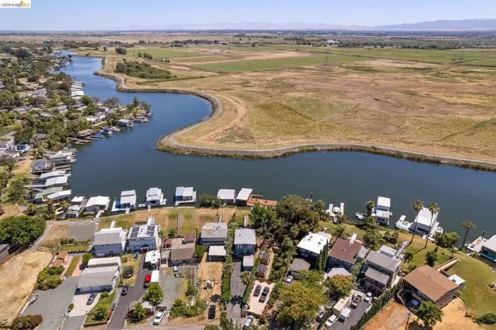 Waterfront properties with private boat docks along a winding river, backed by expansive green and golden fields