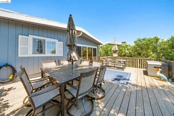 Spacious outdoor deck featuring wood flooring, a surrounding wood railing, and a blue exterior wall with white window shutters