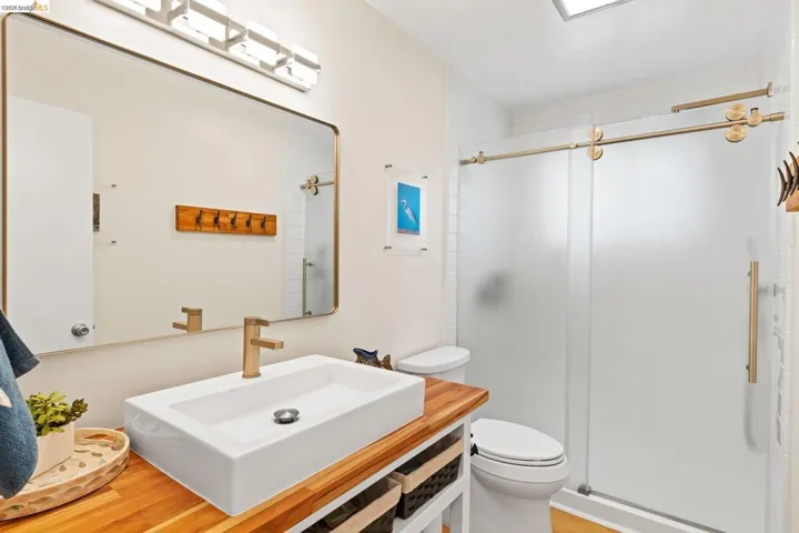 Bathroom featuring a rectangular vessel sink with a gold-tone faucet, wood-finish countertop, and a shower with frosted sliding glass doors and gold-tone hardware