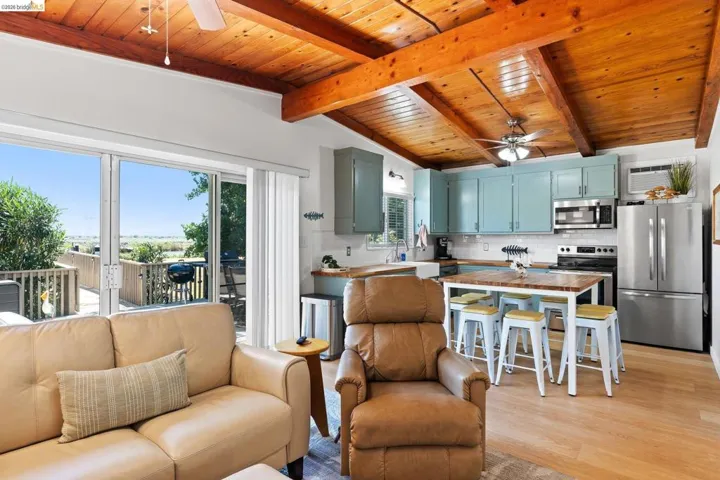 Open-concept living space featuring wood-finish flooring, exposed beam ceiling, and a ceiling fan