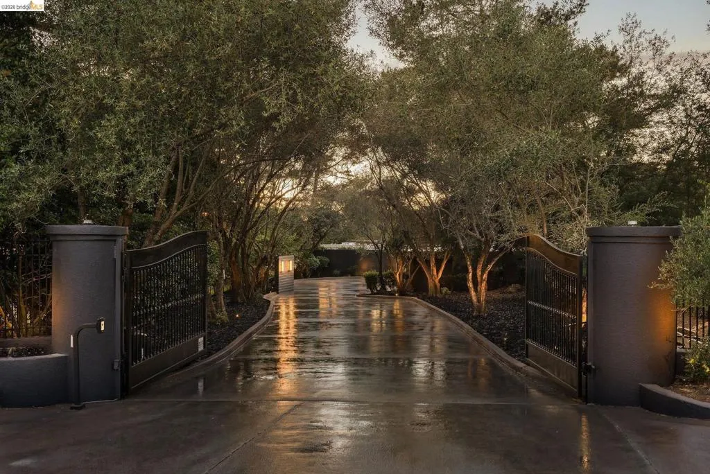 Gated entry featuring wrought iron gates, stucco pillars, and a paved driveway