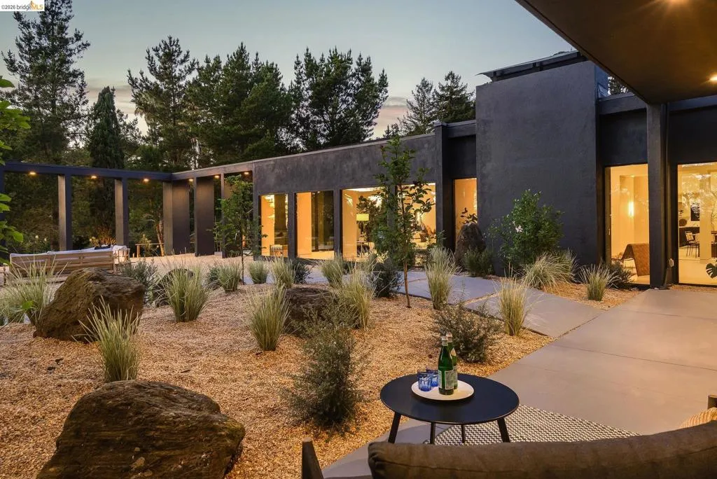 Modern exterior architecture featuring dark-toned stucco, large format windows, and a landscaped yard with decorative gravel, natural boulders, and low-maintenance plantings
