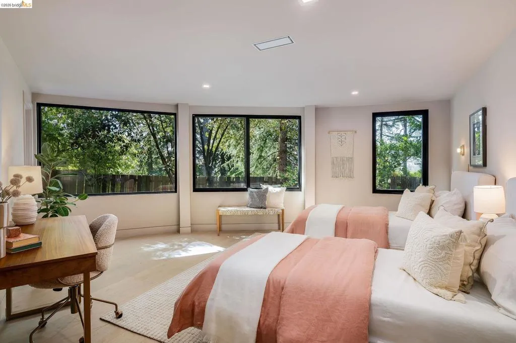 Spacious bedroom featuring multiple large windows with black framing, wood-finish flooring, recessed lighting, and wall-mounted sconces