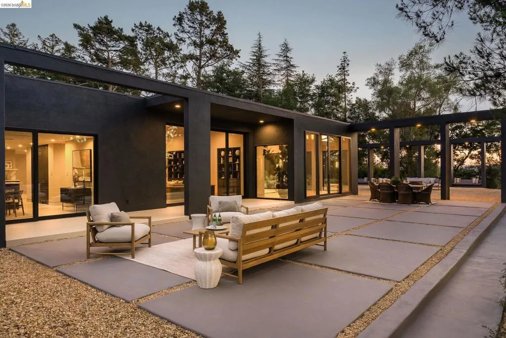 Expansive outdoor patio featuring large concrete pavers, gravel accents, a structured pergola, and multiple floor-to-ceiling glass sliding doors