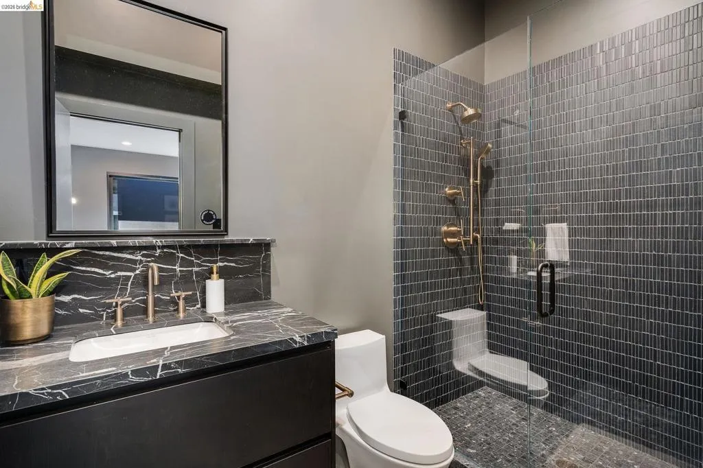 Black vanity with a black and white veined countertop, featuring a rectangular undermount sink and brass-finish fixtures