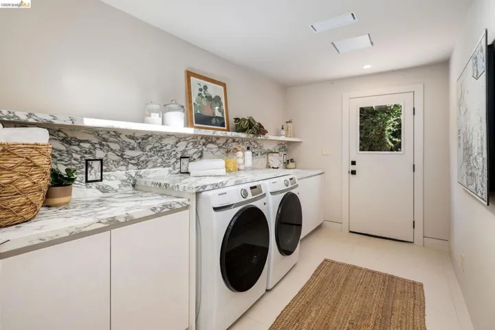 Laundry space featuring a patterned stone countertop and backsplash, white cabinetry, and light-colored flooring