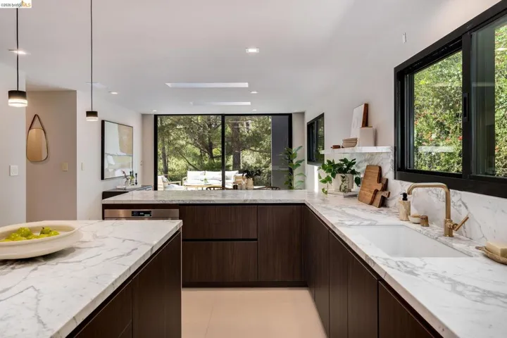 Contemporary kitchen featuring dark wood-finish cabinetry, white veined countertops, an undermount sink with a brass-tone faucet, and recessed lighting