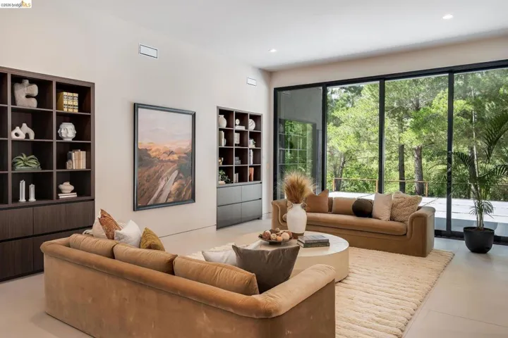 Expansive living area featuring a wall of floor-to-ceiling sliding glass doors, built-in shelving with lower cabinetry, recessed lighting, and light-toned flooring