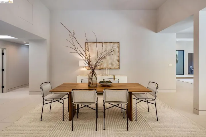 Spacious dining area featuring a light wood-finish table, recessed lighting, high ceilings, light-toned flooring, and a skylight providing natural illumination