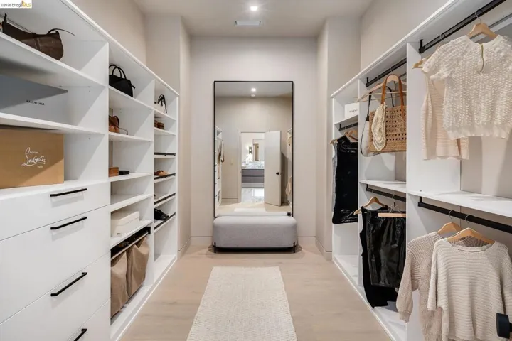 Spacious walk-in closet featuring custom white cabinetry with ample shelving and drawers, built-in hanging rods, wood-finish flooring, and recessed lighting