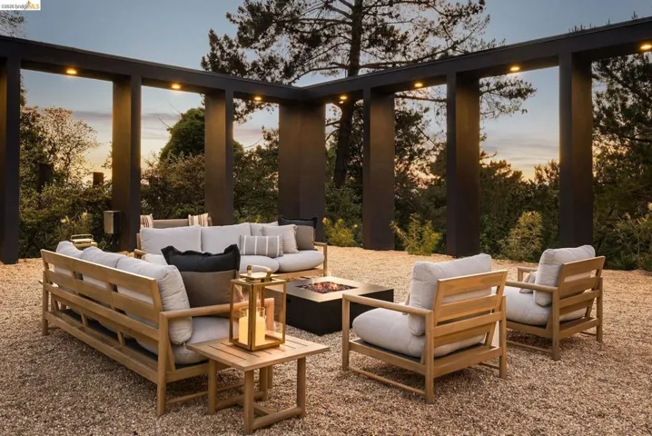 Outdoor lounge area featuring a gravel surface, a built-in fire pit, and a dark-toned perimeter structure with recessed lighting