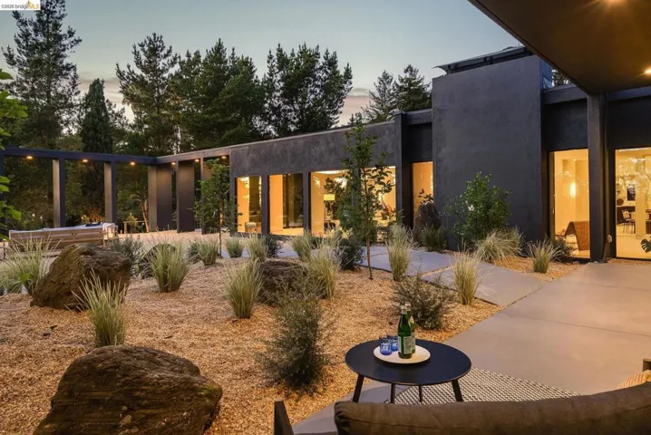 Modern exterior architecture featuring dark-toned stucco, large format windows, and a landscaped yard with decorative gravel, natural boulders, and low-maintenance plantings