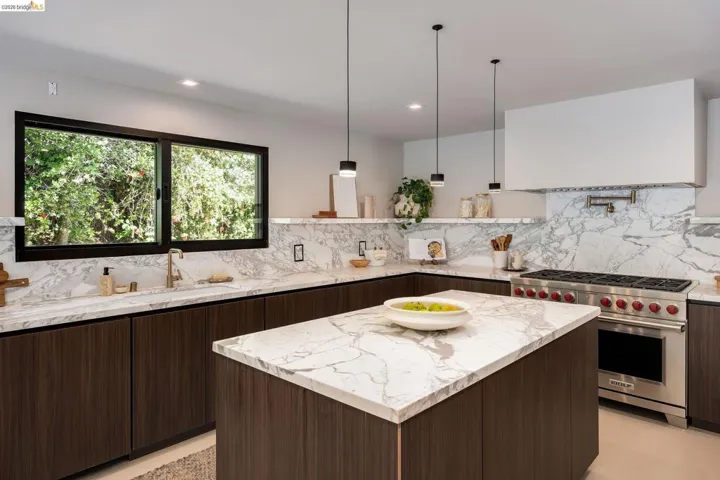 Spacious kitchen featuring an island with a waterfall countertop, dark wood-finish cabinetry, a professional-grade stainless steel range, and a full-height backsplash