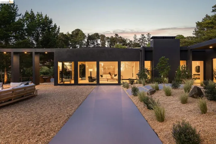 Modern exterior with expansive window walls, a smooth walkway, and a gravel landscape featuring natural boulders and low-maintenance plantings