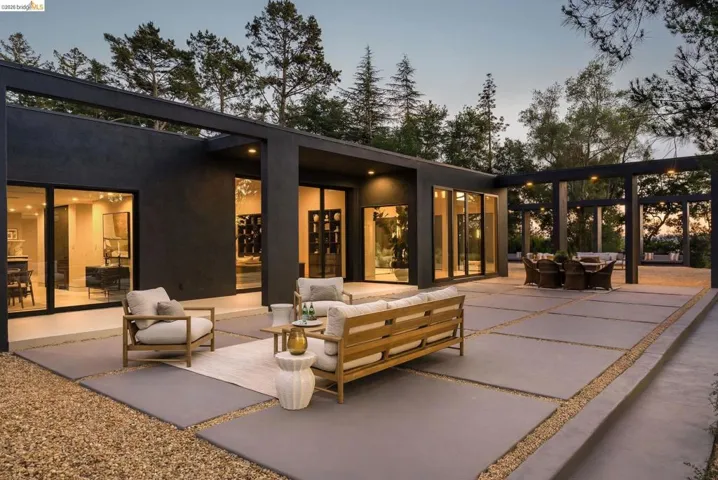 Expansive outdoor patio featuring large concrete pavers, gravel accents, a structured pergola, and multiple floor-to-ceiling glass sliding doors