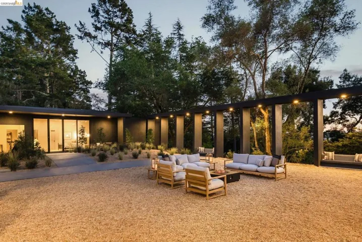 Spacious outdoor courtyard featuring a gravel surface, a pergola with integrated lighting, and a modern structure with sliding glass doors