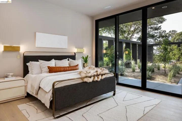 Full-height sliding glass doors opening to an exterior patio with landscaping, light wood-finish flooring, and recessed ceiling lighting