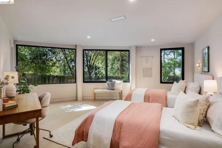 Spacious bedroom featuring multiple large windows with black framing, wood-finish flooring, recessed lighting, and wall-mounted sconces