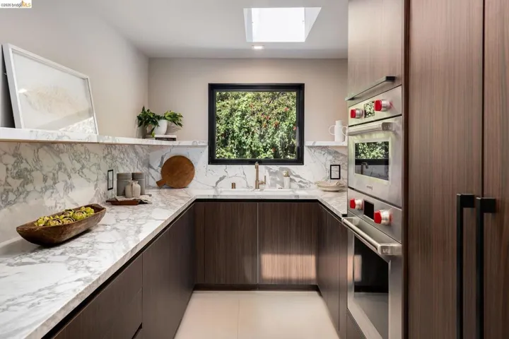 Contemporary kitchen featuring wood-finish cabinetry, light-toned stone countertops, and a full-height stone backsplash