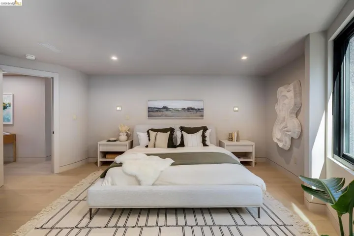 Spacious bedroom featuring light-toned wood-finish flooring, recessed ceiling lighting, and a large window with a black frame