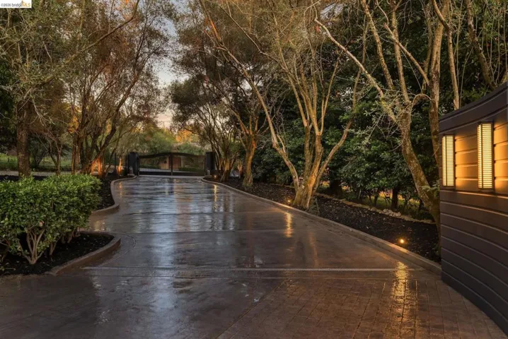 Curved paver driveway with integrated landscape lighting leading to a dark metal entry gate
