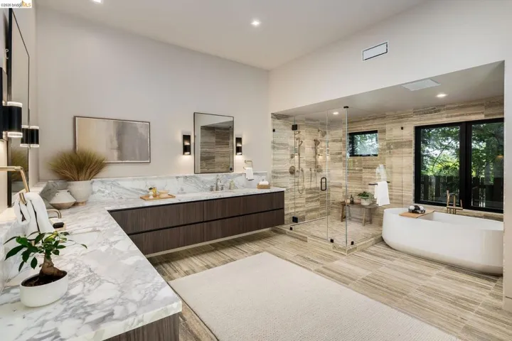 Spacious bathroom featuring a dual vanity with a stone countertop, a glass-enclosed shower, a freestanding soaking tub, and large format tile flooring