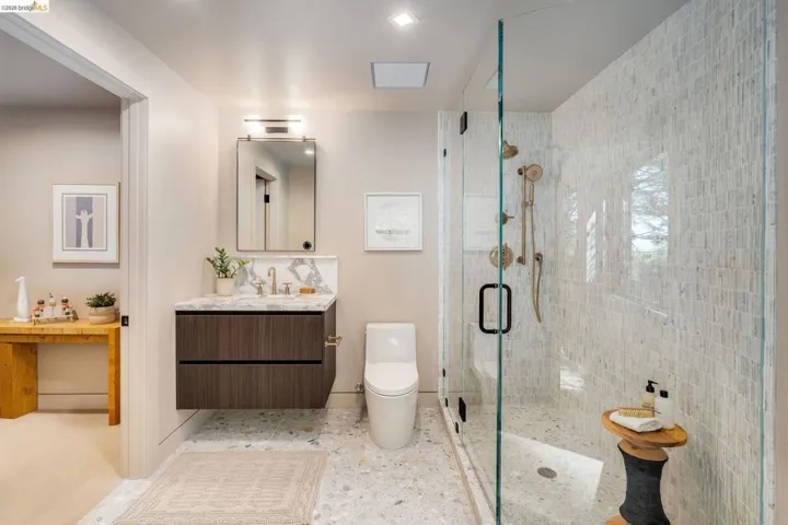 Bathroom featuring a floating wood-finish vanity with a stone countertop and backsplash, a glass-enclosed shower with mosaic tile, and multi-tone terrazzo flooring