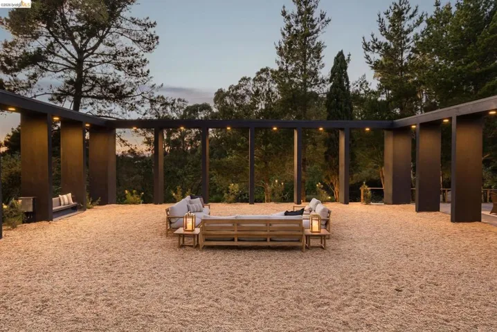 Expansive outdoor patio area featuring a light-colored gravel surface and a dark-toned pergola structure