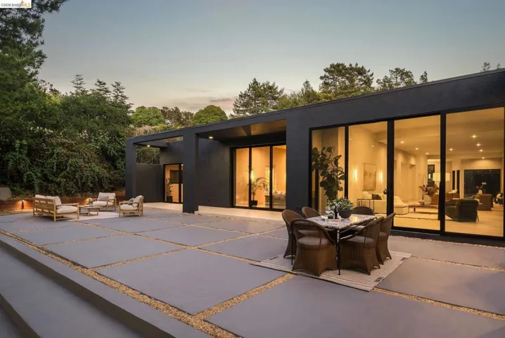 Expansive concrete patio with gravel fill, featuring a modern dark-colored home with large glass sliding doors and an outdoor covered walkway
