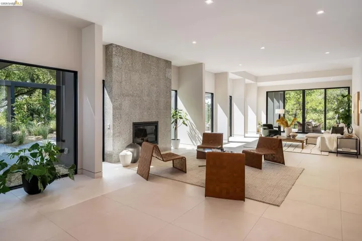 Spacious living area featuring expansive windows, recessed lighting, a textured stone fireplace, and light-toned tile flooring throughout