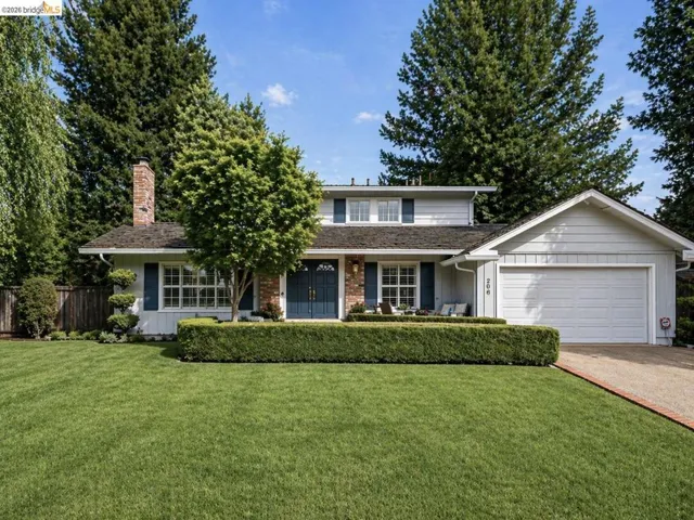 Traditional-style 4bed/3bath residence featuring a prominent front lawn, established landscaping, and a brick chimney accent