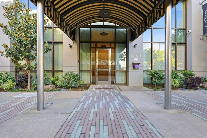 Contemporary building entrance featuring a striped metal awning and a patterned paver walkway