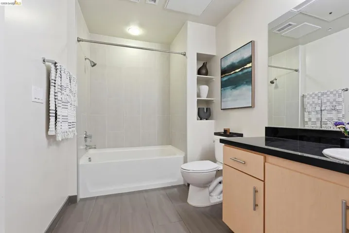Bathroom featuring a full tub with shower, tiled surround, and wood-finish flooring