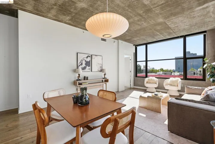 Spacious living area featuring a wood-finish dining table, large window wall, exposed concrete ceiling, and light wood-finish flooring