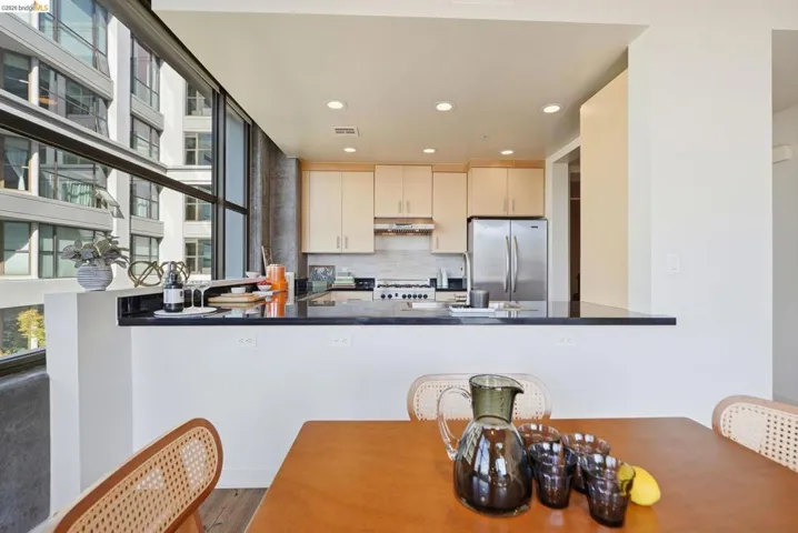 Kitchen featuring light wood cabinetry, stainless steel appliances, a black countertop breakfast bar, recessed lighting, and expansive window walls