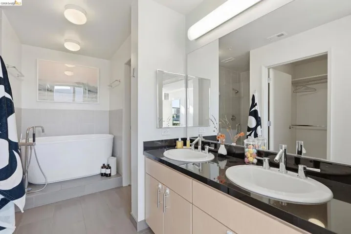 Bathroom featuring a dual vanity with light wood-finish cabinetry, dark stone countertop, and chrome fixtures