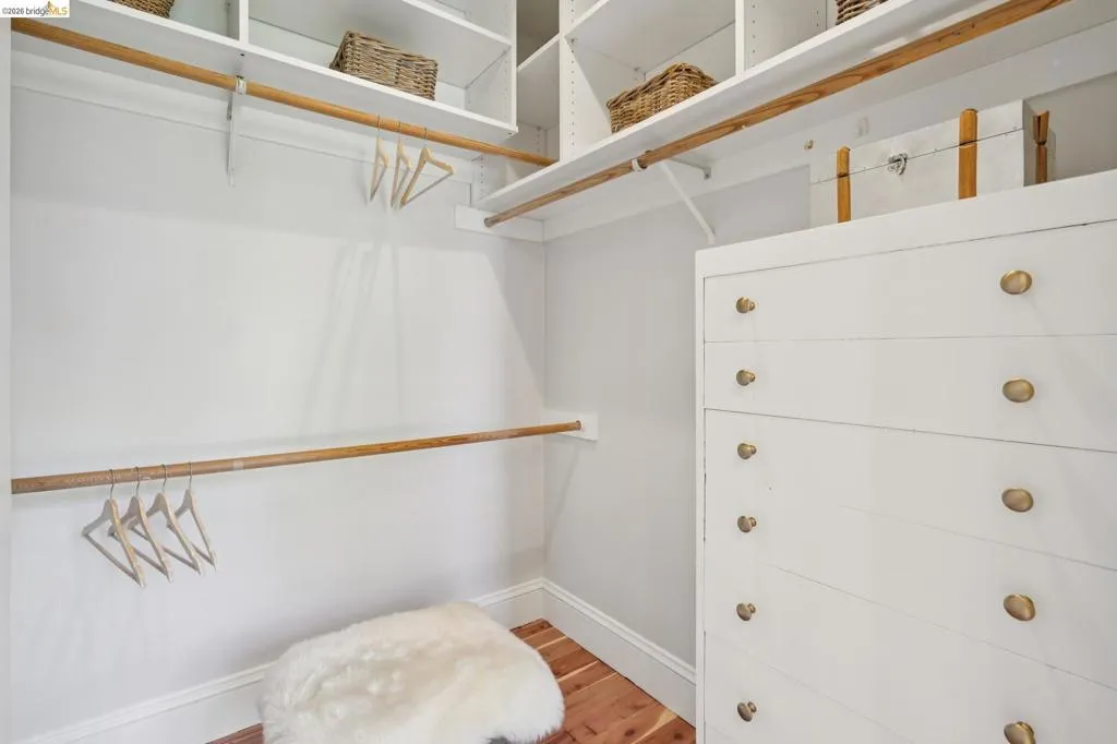 Walk-in closet featuring built-in white shelving, multiple hanging rods, a white built-in dresser with brass-finish knobs, and cedar flooring.