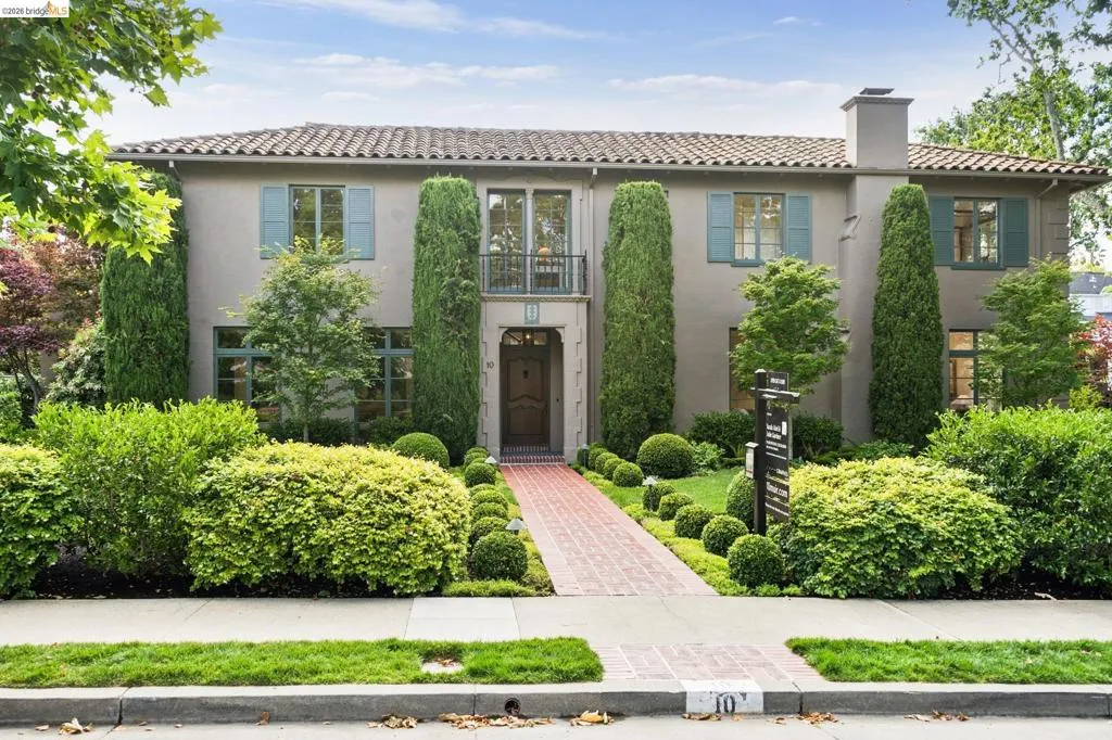 Stucco exterior with a tile roof, featuring a brick pathway surrounded by structured landscaping