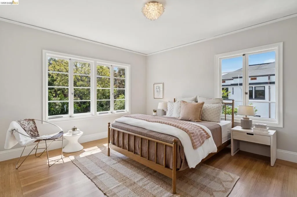 Light-filled room featuring wood-finish flooring, two large windows with white trim, a built-in ceiling light fixture, and crown molding