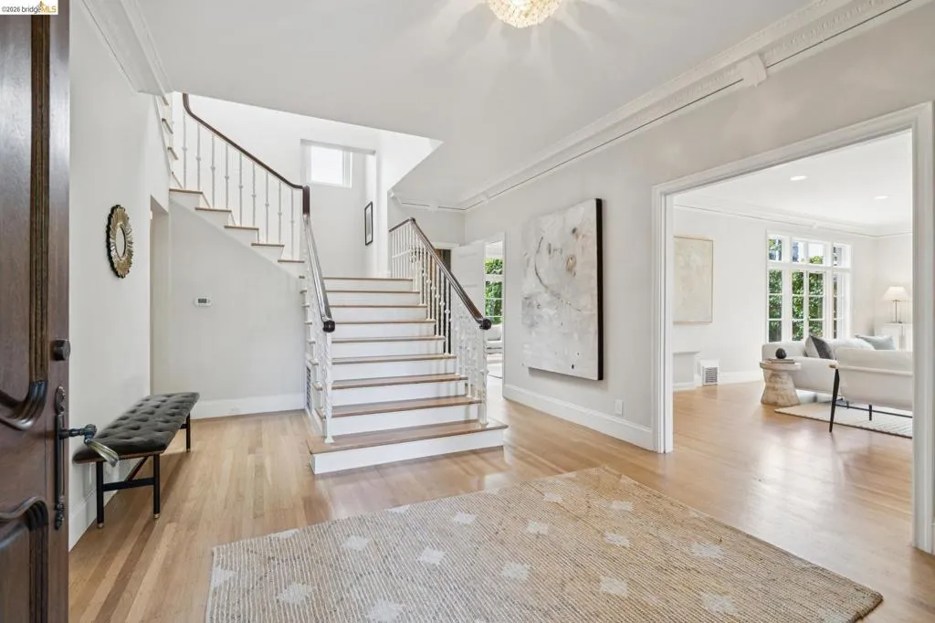 Entry foyer featuring wood-finish flooring, a grand staircase with dark wood handrails and white balusters, and crown molding