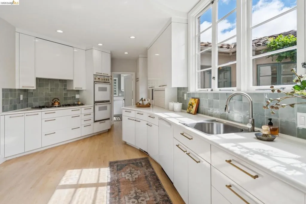 Modern kitchen featuring white cabinetry, light countertops, integrated double ovens, and a stainless steel sink