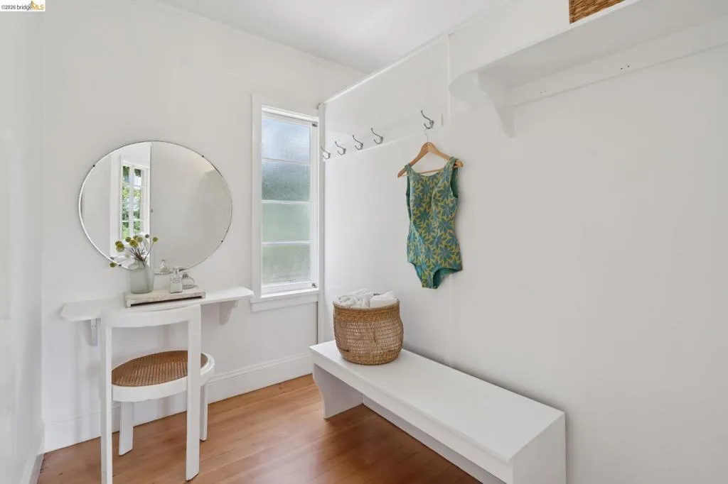 Entryway featuring wood-finish flooring, a built-in white bench, wall-mounted coat hooks, and a built-in floating shelf with a round wall mirror